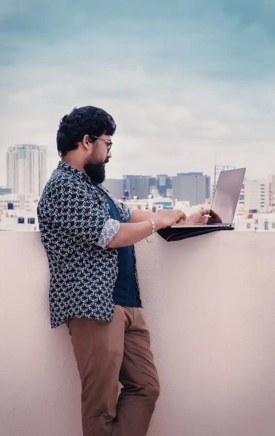 A person working on a laptop with the Bengaluru skyline behind